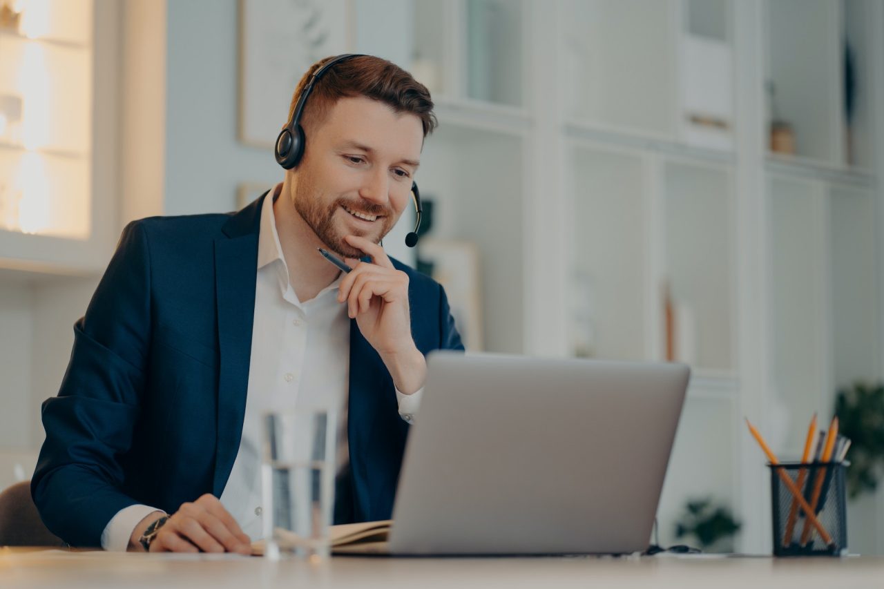 professional-male-operator-works-in-callcenter-uses-headset-and-laptop-computer-talks-on-video-call